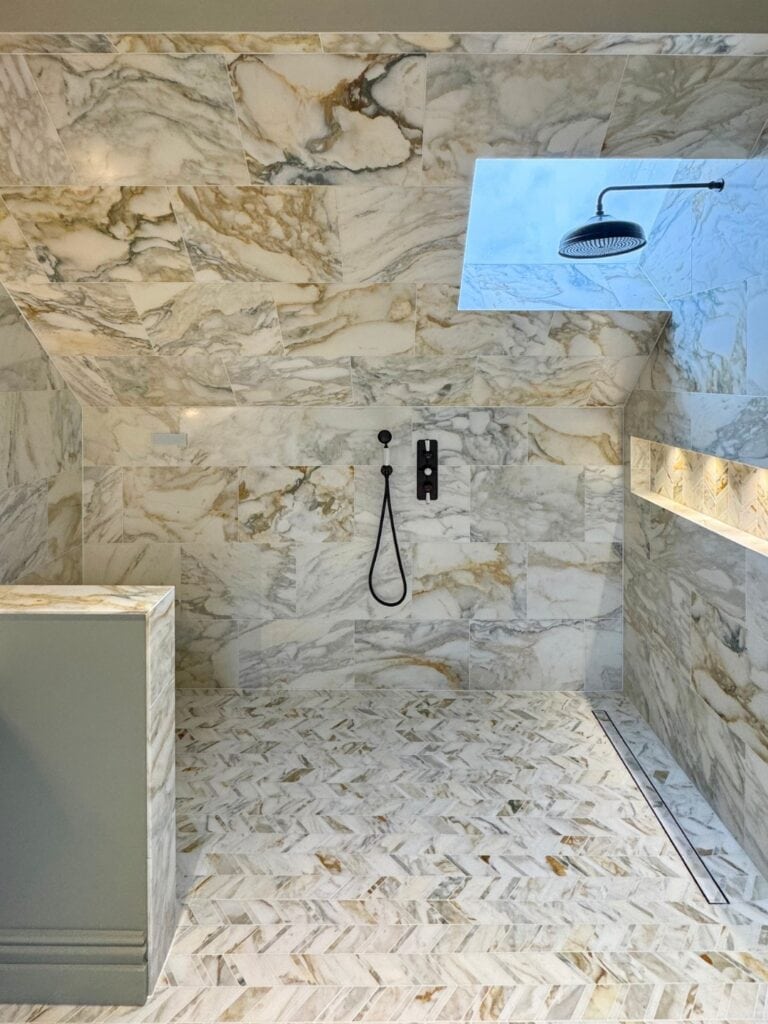 Marble steam room with built-in bench, rainfall shower and illuminated shelf.