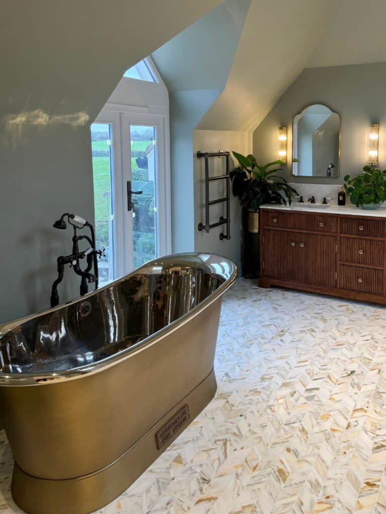 Metal freestanding bath beside a wood vanity in the Rudgwick bathroom.