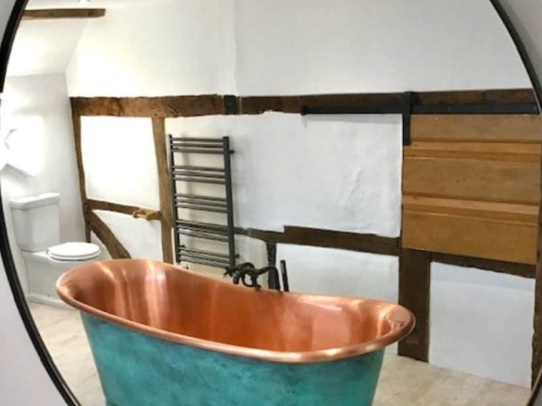 Vintage copper bathtub in rustic bathroom with exposed wooden beams and white walls.