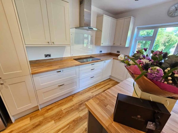 White shaker kitchen with wood worktops beside a window